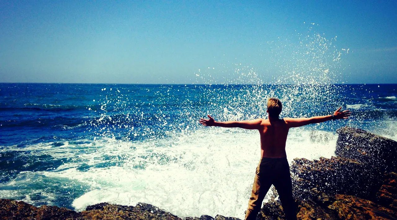 A person standing on a rock facing the sea with his arms outstretched